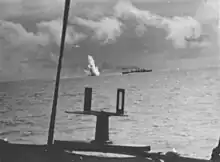 An underwater explosion sends water flying through the air shortly behind a speeding warship
