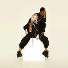 Khalid and Eilish are seen sitting down, posing for a photo.