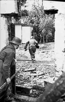 One man running across open space while a second peeps around a doorway