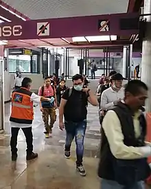 Multiple people, some wearing masks and others without, walk through a lobby