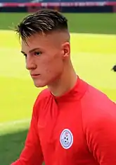 A young white man, wearing a red football kit.