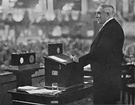 President Harding stands before a crowd with radio broadcasting equipment in front of him.