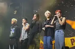 A group photo of SB19 on stage with each member holding a handheld microphone.