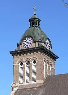 Steeple with copper dome, topped by cross; clock dials face in four directions