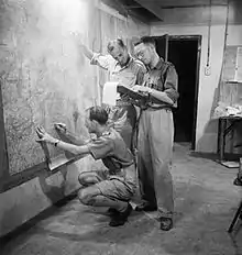 British staff officers plot positions on large wall charts during the invasion of Sicily