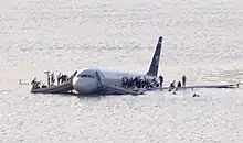 A partially submerged Airbus A320 with front emergency slides deployed and people standing on its wings