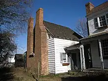 Photo of the one and one-half-story white wooden building with double brick chimneys.
