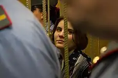 A woman with brown hair and a floral shirt. Her view is obstructed by two uniformed officers standing in front of her.